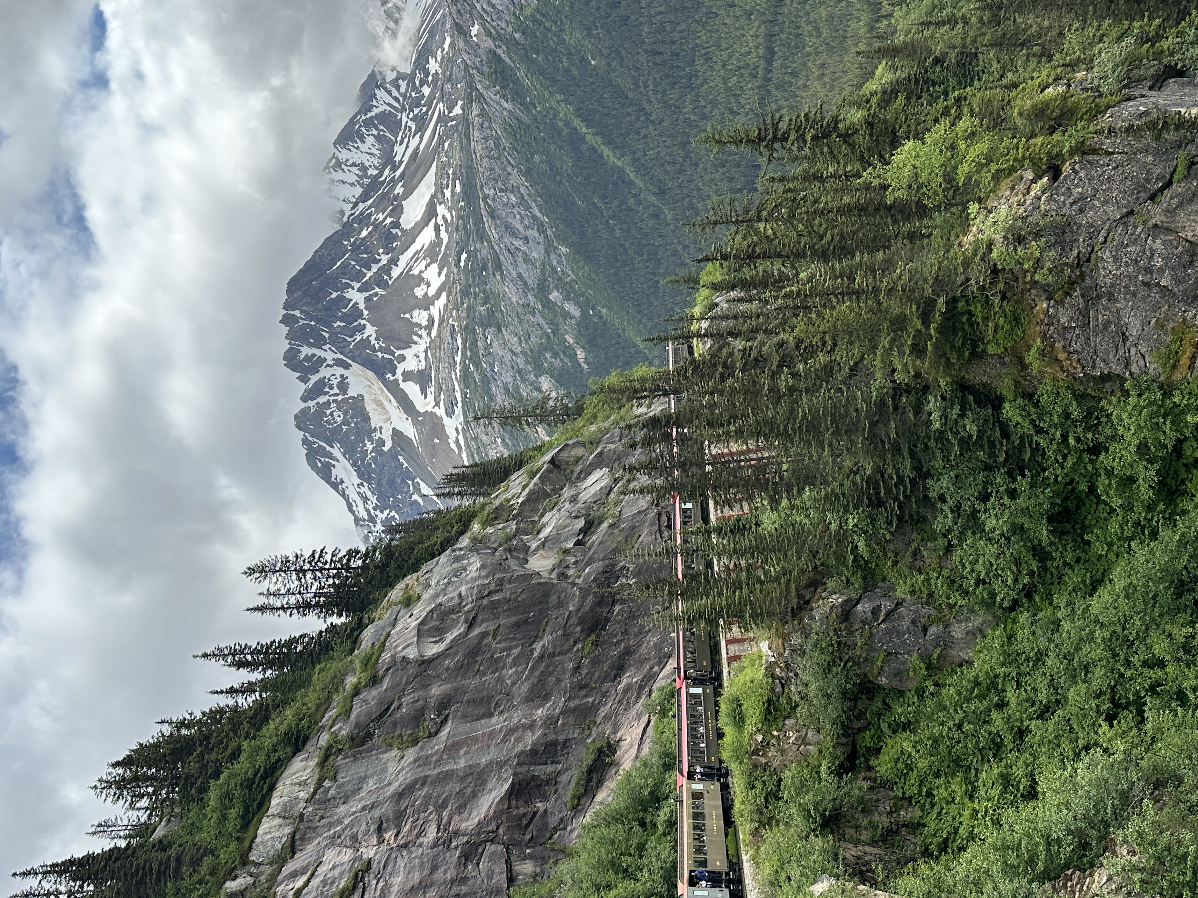 Vintage narrow-gauge train climbing a ledge above an Alaskan valley